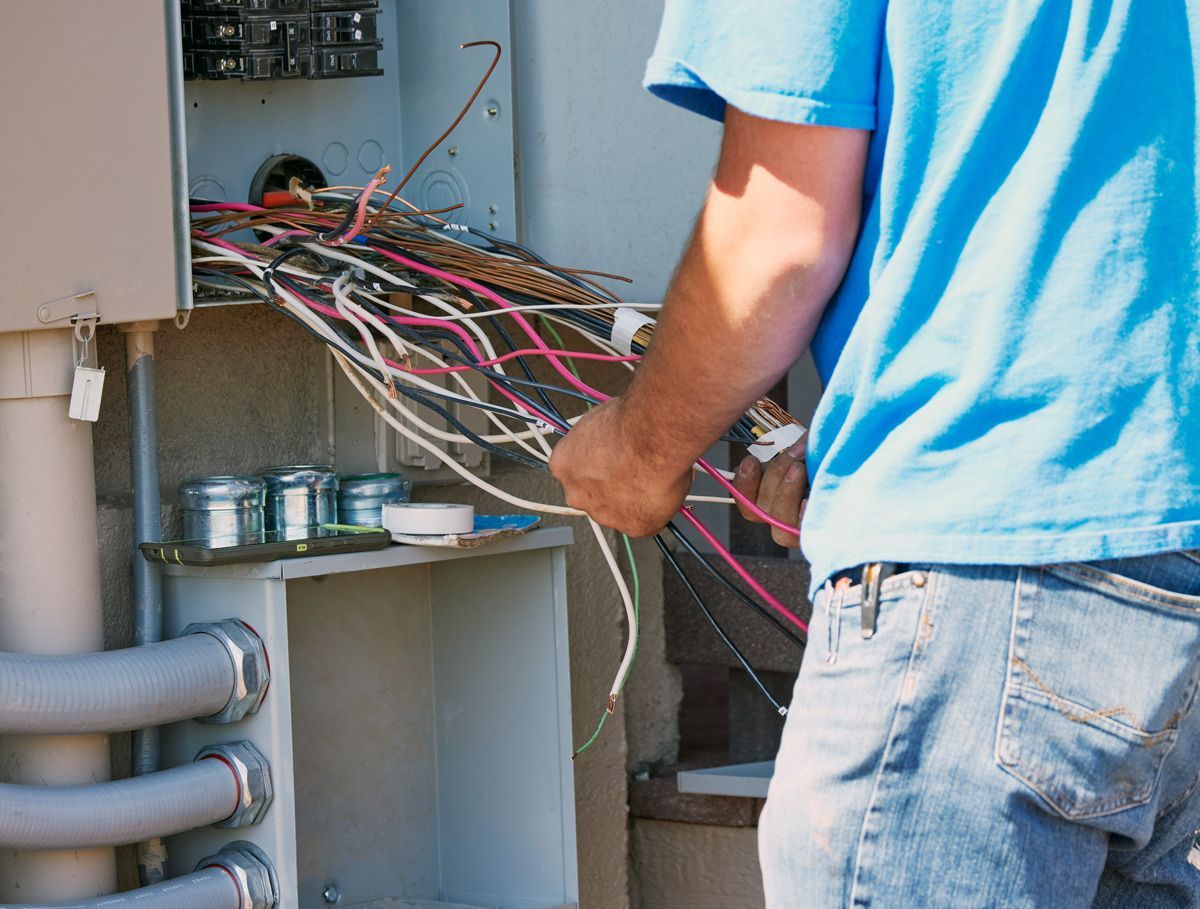 Person in blue shirt working on electrical wiring in an outdoor electrical box.