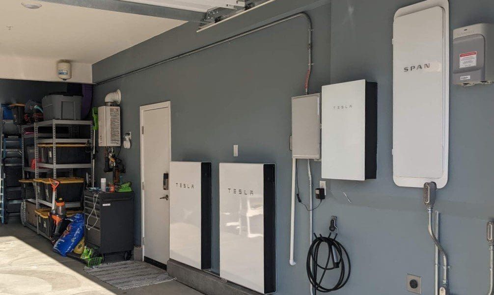 Garage interior with solar battery storage units on a gray wall, plus charging cables.