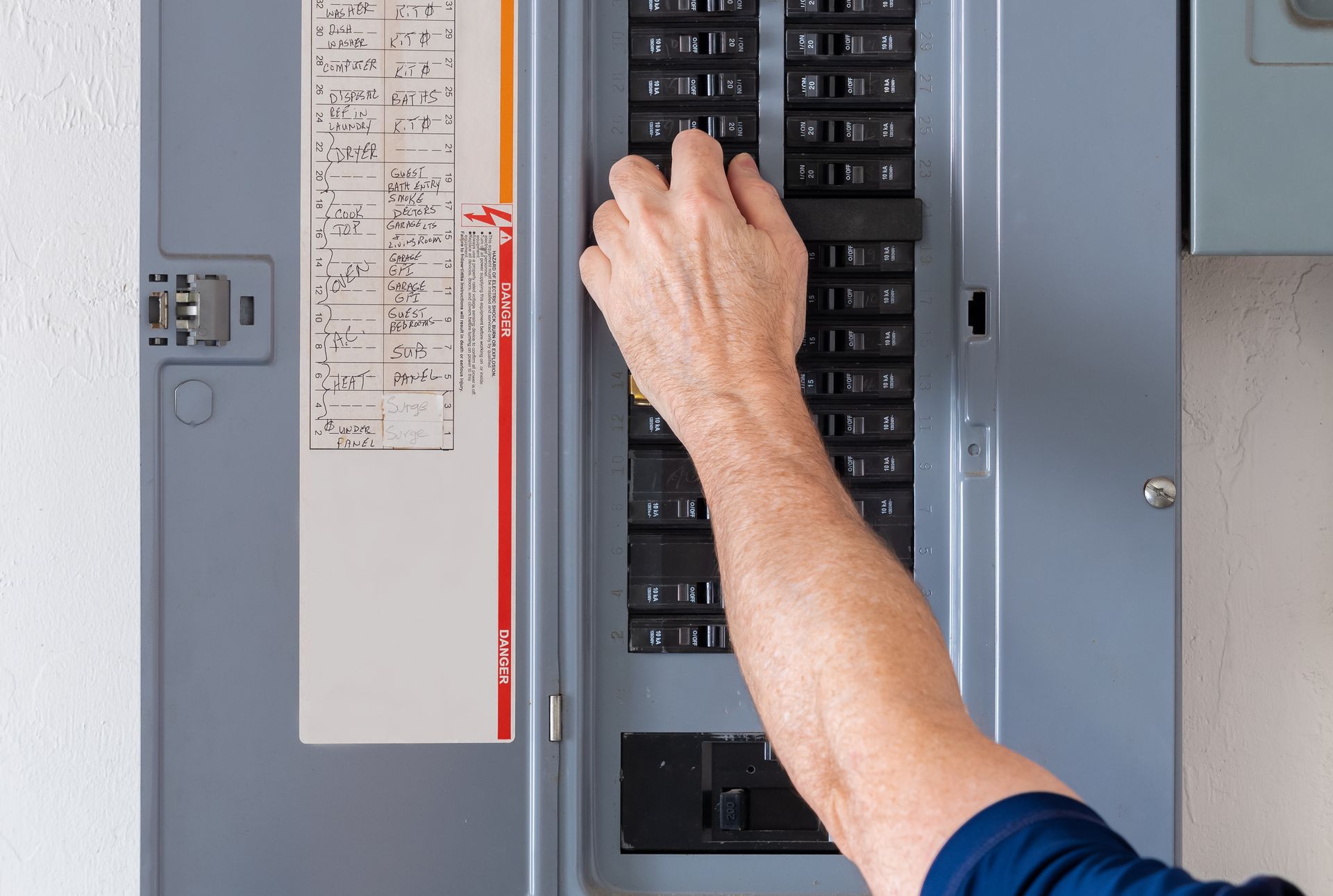 Hand flipping a circuit breaker in a gray electrical panel.