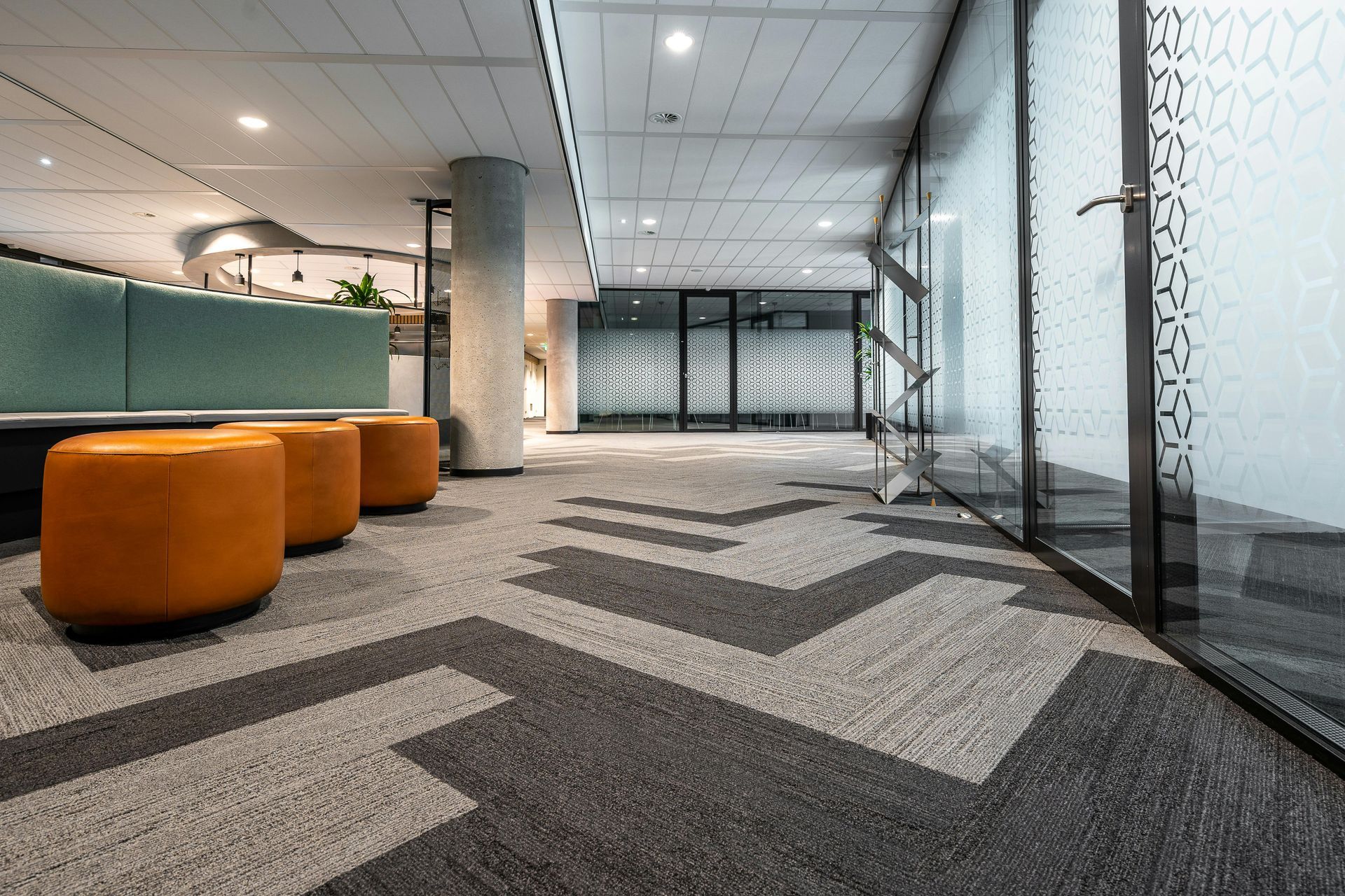Modern office lobby with orange ottomans, patterned carpet, and glass walls.