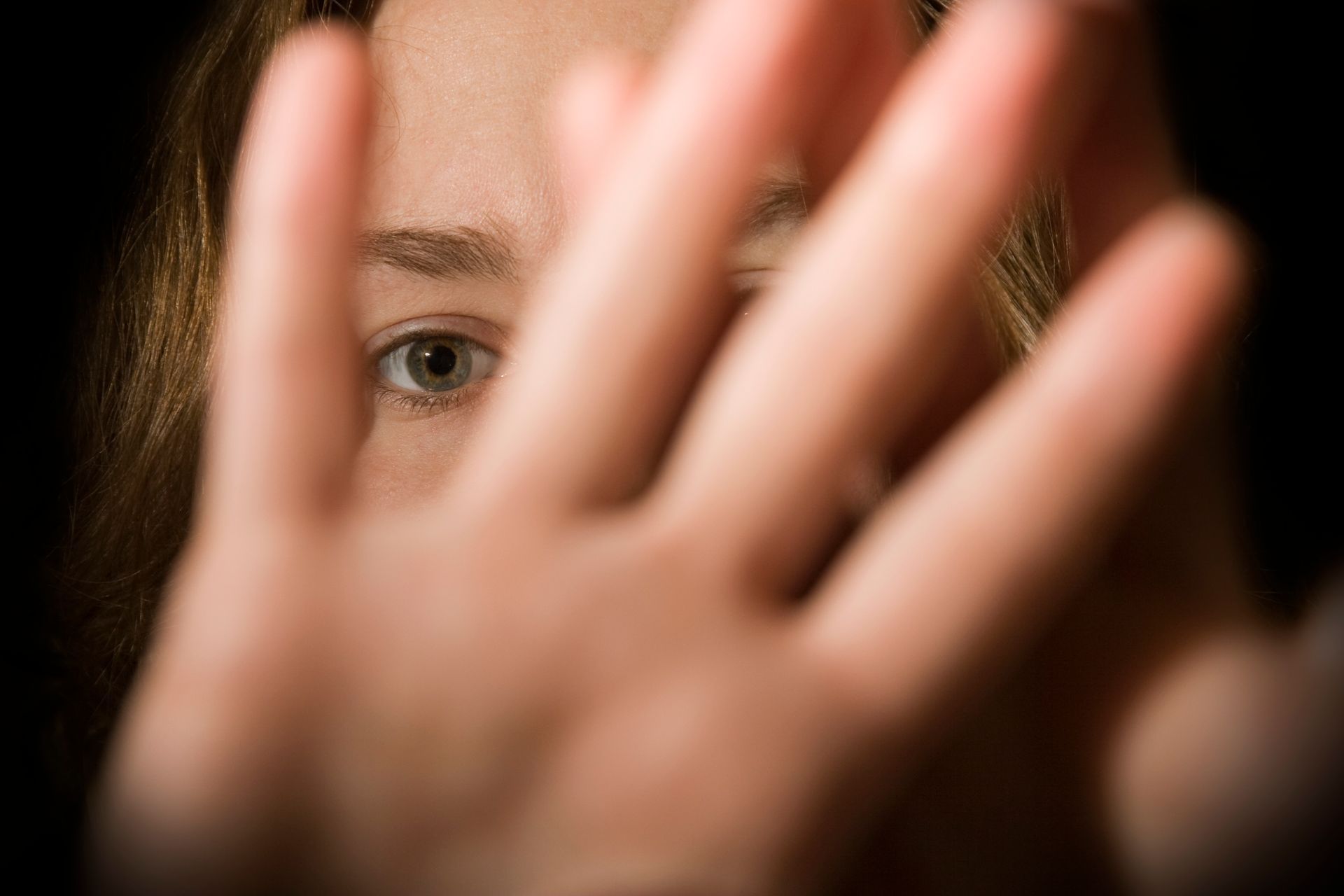 Il volto di una donna sbuca da dietro la sua mano. Sembra spaventata, con gli occhi spalancati e uno sfondo scuro.