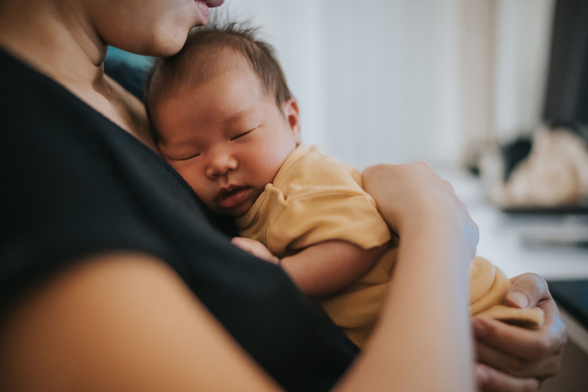 Neonato che dorme pacificamente sul petto di una persona, entrambi in una stanza ben illuminata.