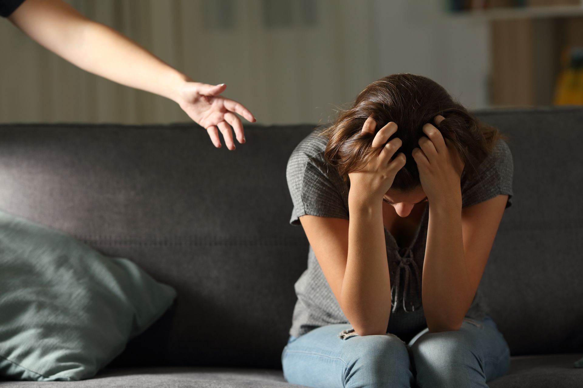 Una donna è seduta su un divano con la testa tra le mani e una mano tesa per aiutarla.