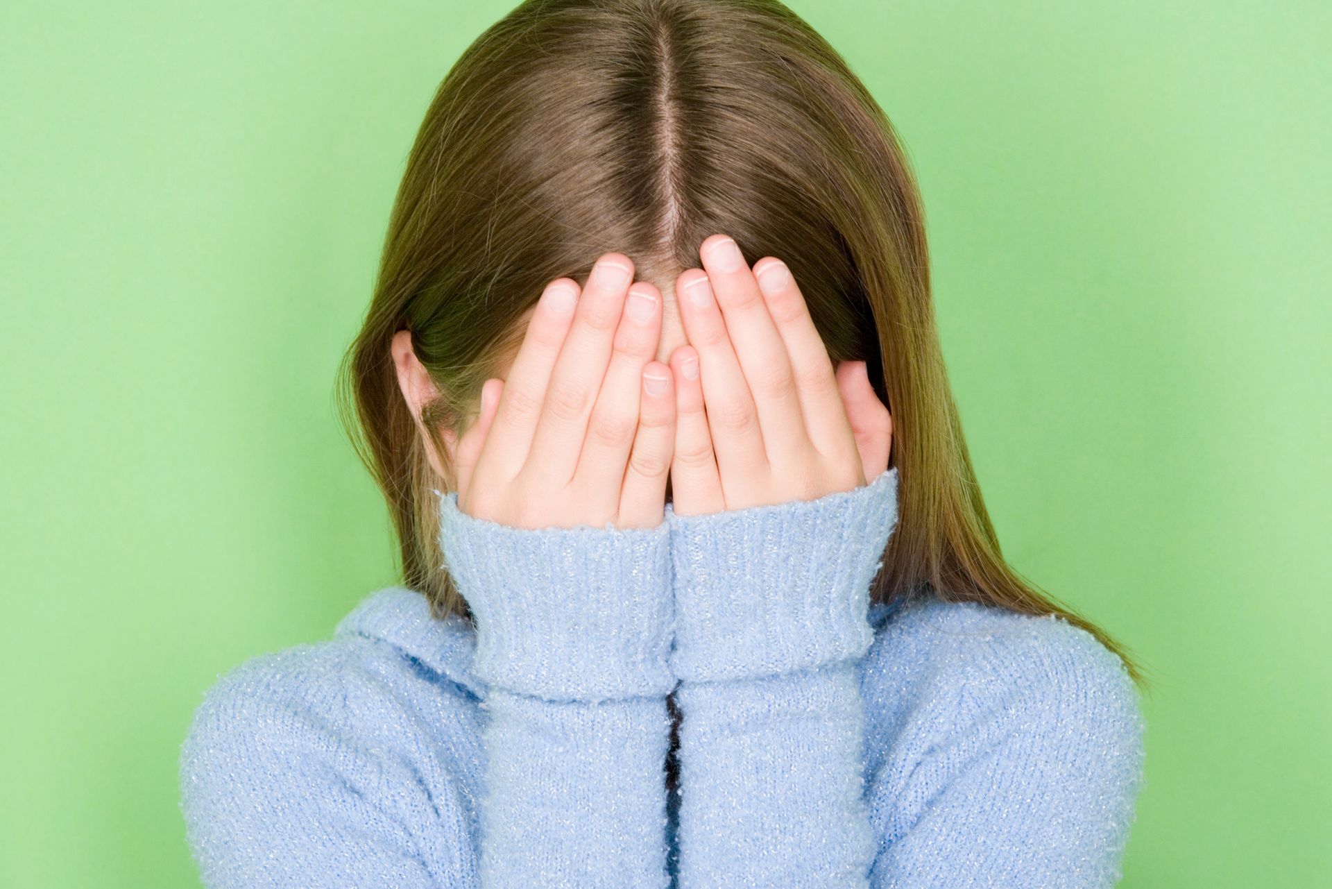 Una ragazza con un maglione blu si copre il viso con le mani, su sfondo verde.