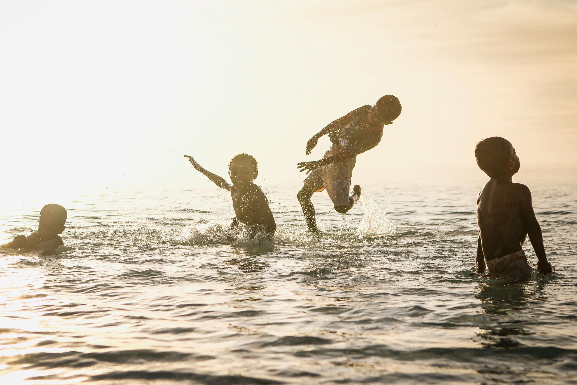 Bambini che giocano in acqua illuminata dal sole, spruzzando e divertendosi.