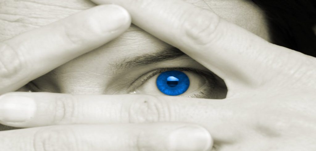 L'occhio azzurro di una persona che spunta tra le dita.