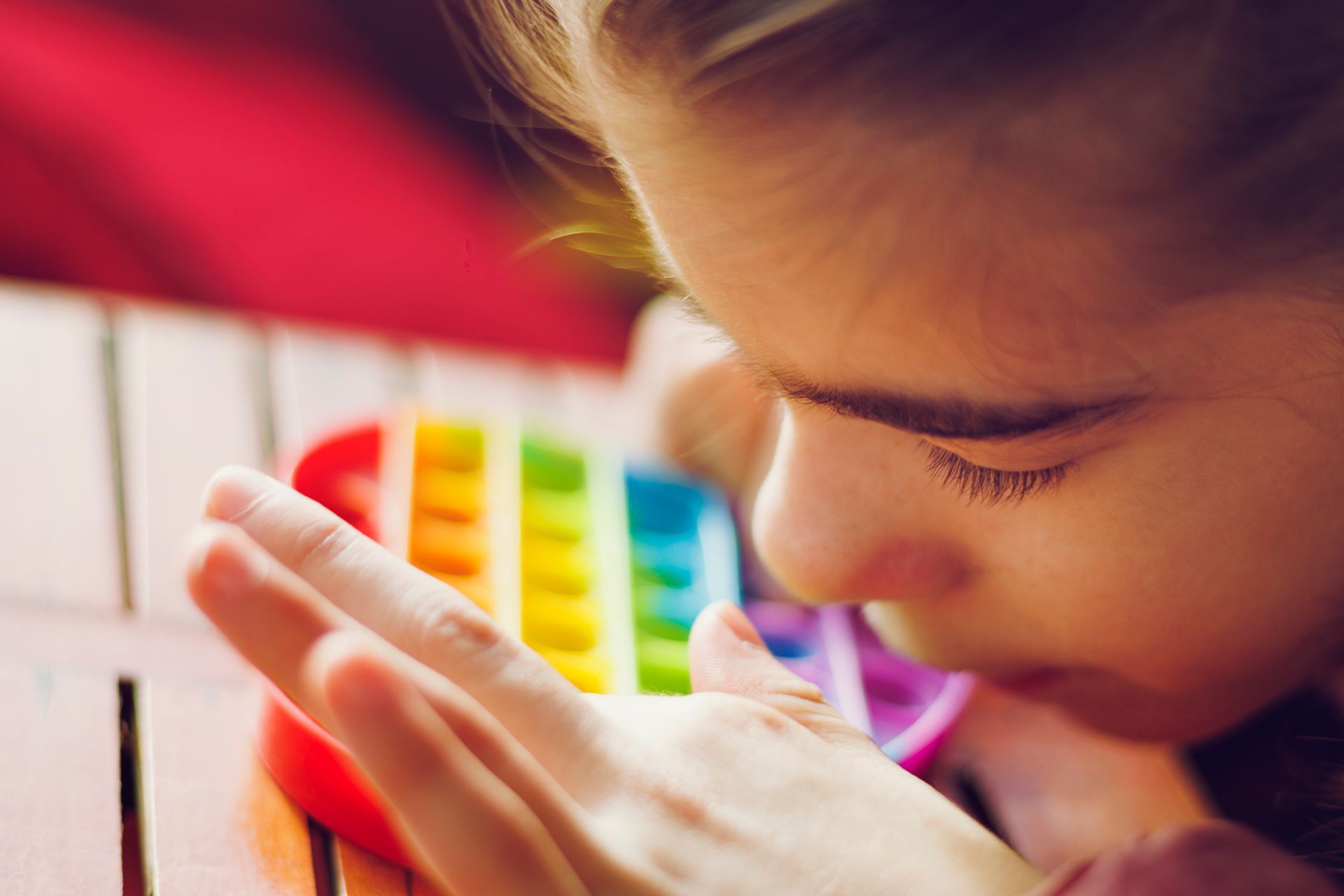Ragazza ipovedente che preme le bolle su un Pop It arcobaleno, primo piano.