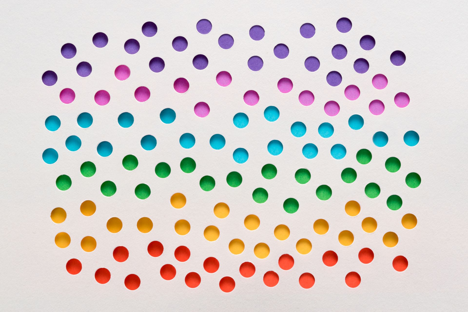 Rows of colorful circles in rainbow order, punched out of white paper.