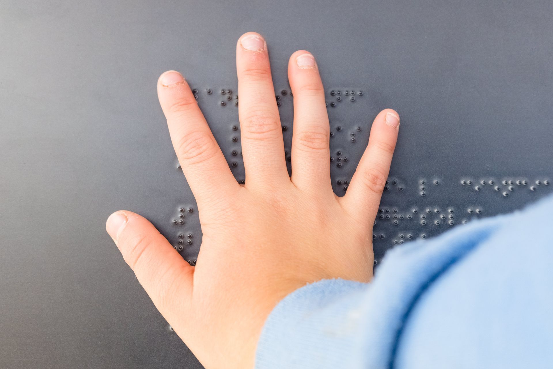 La mano di un bambino su una superficie con il braille, che esplora i punti con le dita.