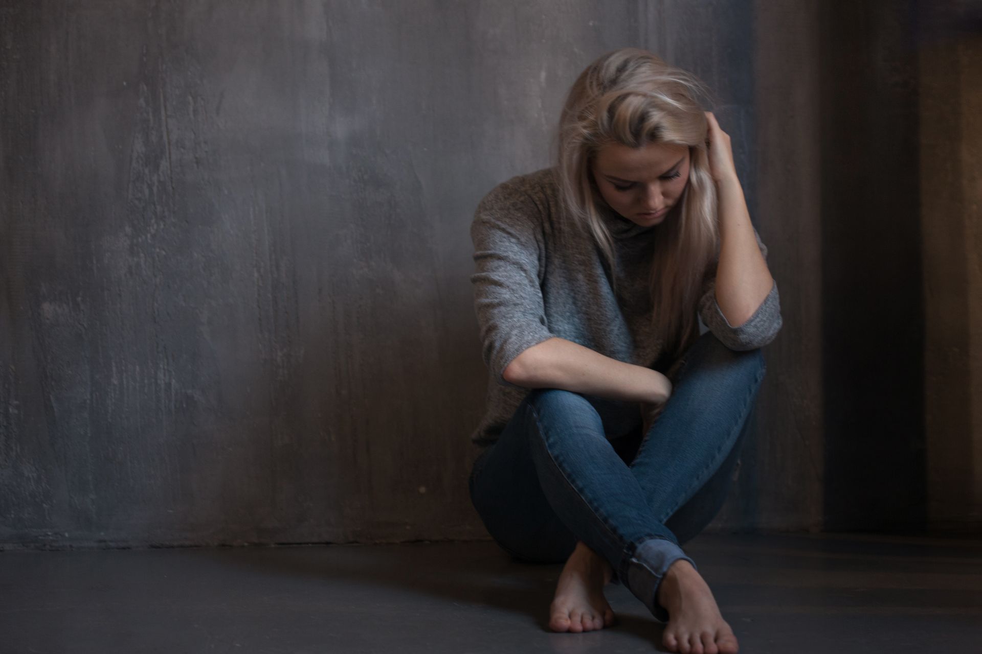 A woman is sitting on the floor with her legs crossed and her head in her hands.