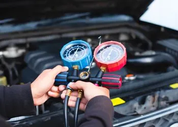 A person is holding two gauges in front of a car engine.