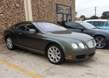 A bentley is parked in a parking lot in front of a building.