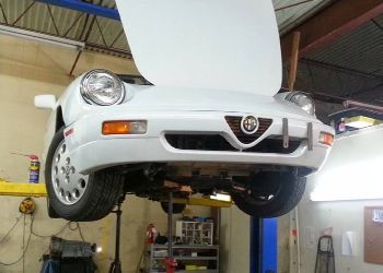 A white car with the hood up is on a lift in a garage.