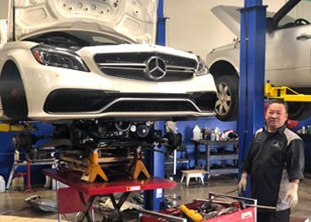 A man is standing next to a mercedes on a lift in a garage.