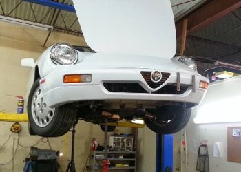 A white car with the hood open is on a lift in a garage.