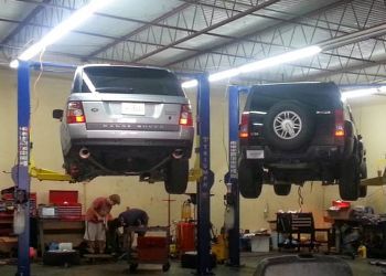 Two cars are sitting on a lift in a garage.