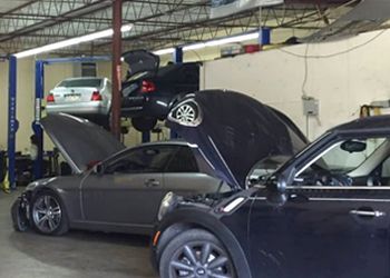 Two cars are in a garage with their hoods open.