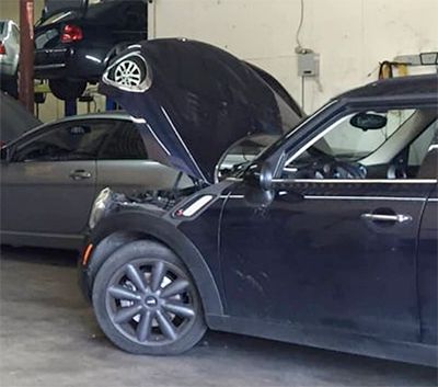 A black mini cooper with its hood up in a garage