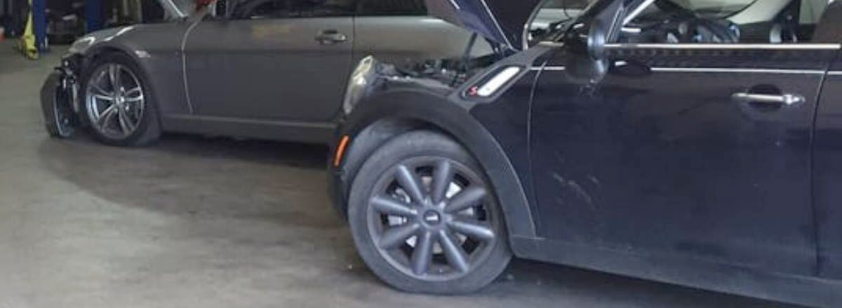 Two cars are parked next to each other in a garage with the hood open.