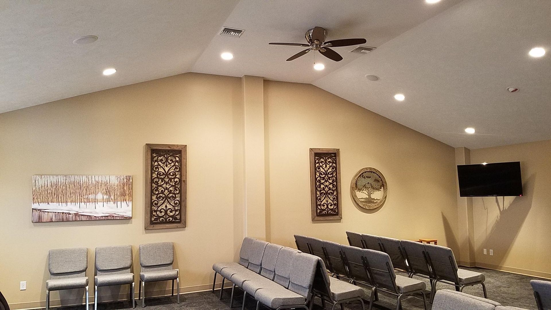 Beige-walled room with chairs, art, a TV, and a ceiling fan.