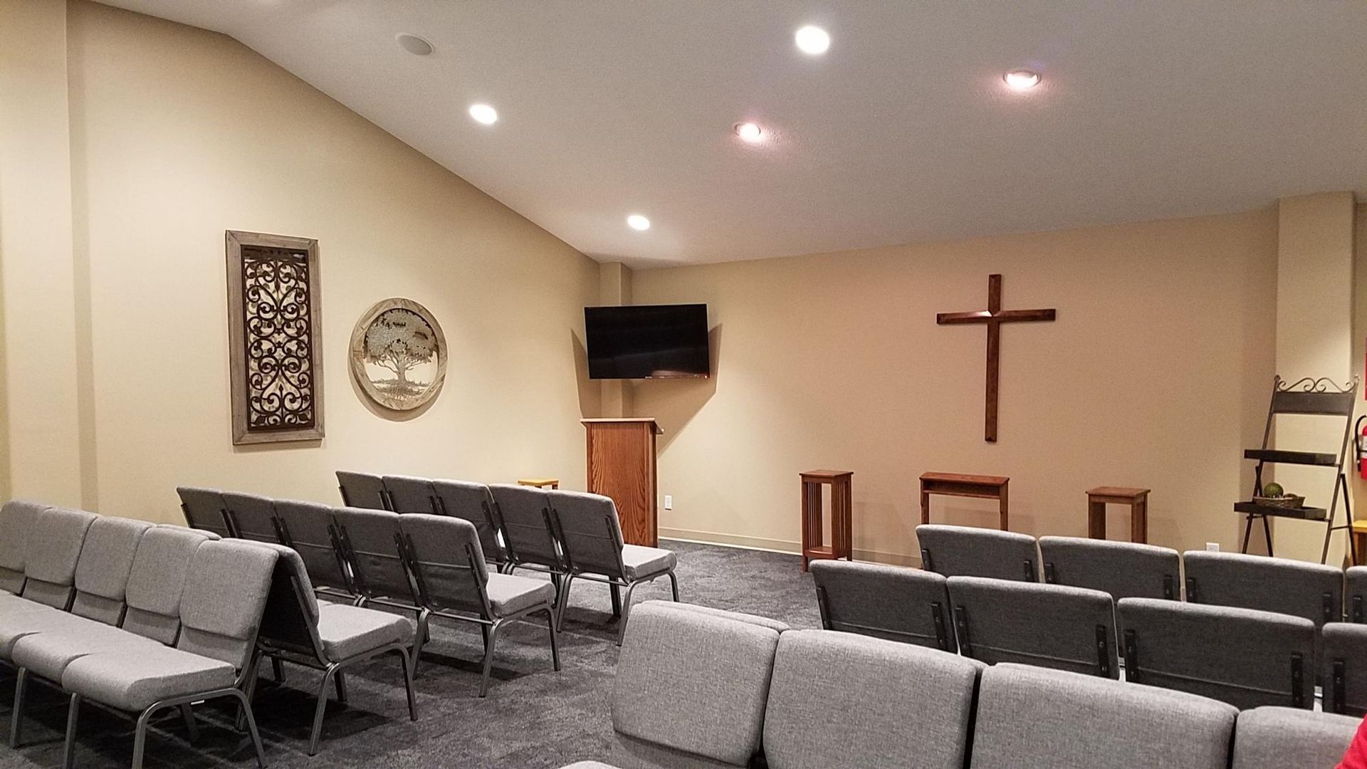 Interior of a chapel with rows of gray chairs facing a wooden cross on the wall.