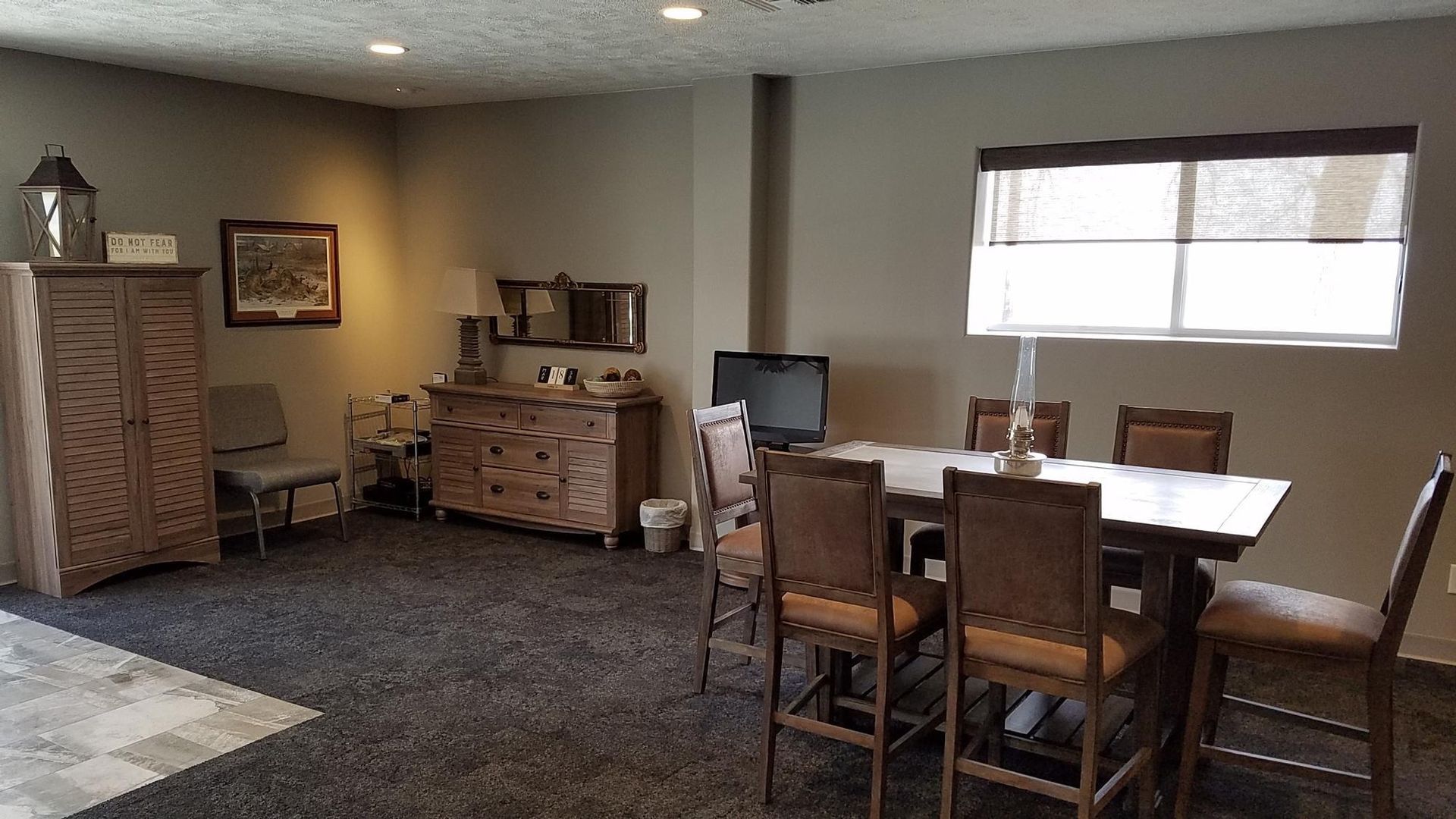 A dining area with a table, chairs, and a window. There's also a cabinet and dresser on the side.