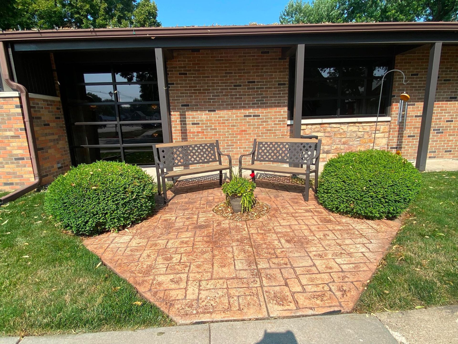 Brick building with two benches, bushes, and a brick patio.