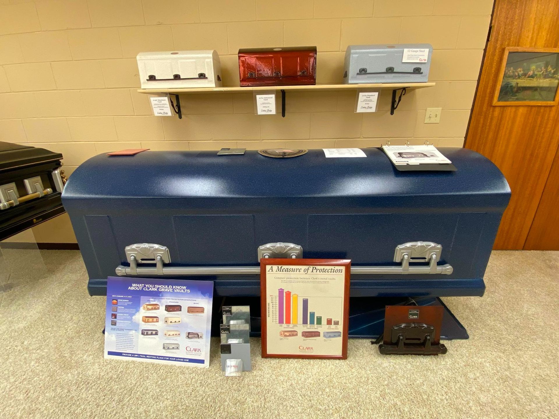 A room displays coffins of various colors on shelves and the floor, along with informational materials.