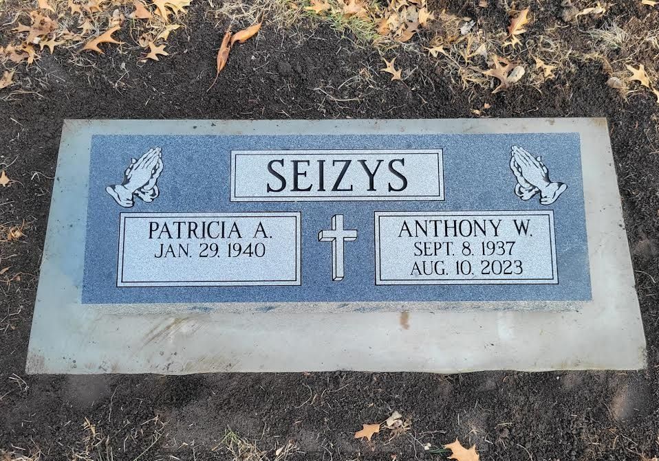 Headstone for Patricia A. (1940- ) and Anthony W. Seizys (1937-2023). Blue panels with praying hands and a cross.