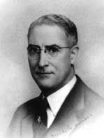 Man wearing glasses and suit, looking towards the viewer.