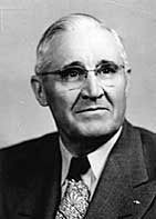 Portrait of an older man with glasses, wearing a suit and tie.
