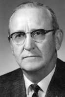Man in glasses, suit, and tie. He has a serious expression.
