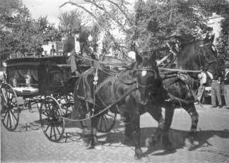 Horse-drawn hearse carrying a coffin, likely a funeral procession on a city street.