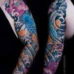 A woman has a full sleeve tattoo of a fish and flowers on her arm.