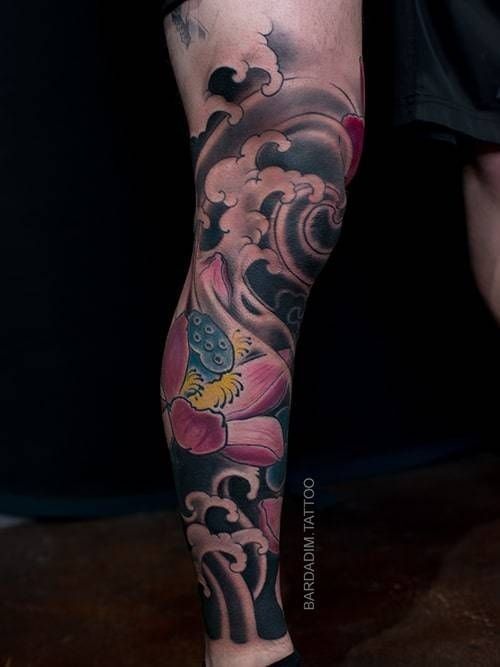 A person has a tattoo on their leg of a lotus flower and waves.