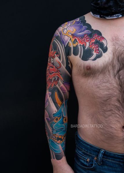 A shirtless man with a colorful tattoo on his arm and chest.