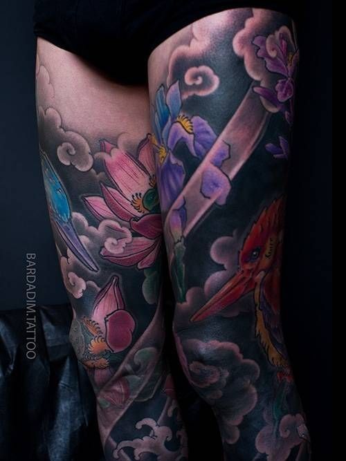 Leg tattoos with colorful lotus flowers, iris, bird, and clouds.
