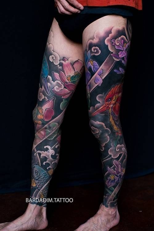 Leg tattoos in vibrant colors featuring flowers, clouds, and a phoenix against a dark background.