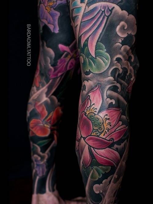 Leg tattoos with colorful lotus flowers, clouds, and waves.