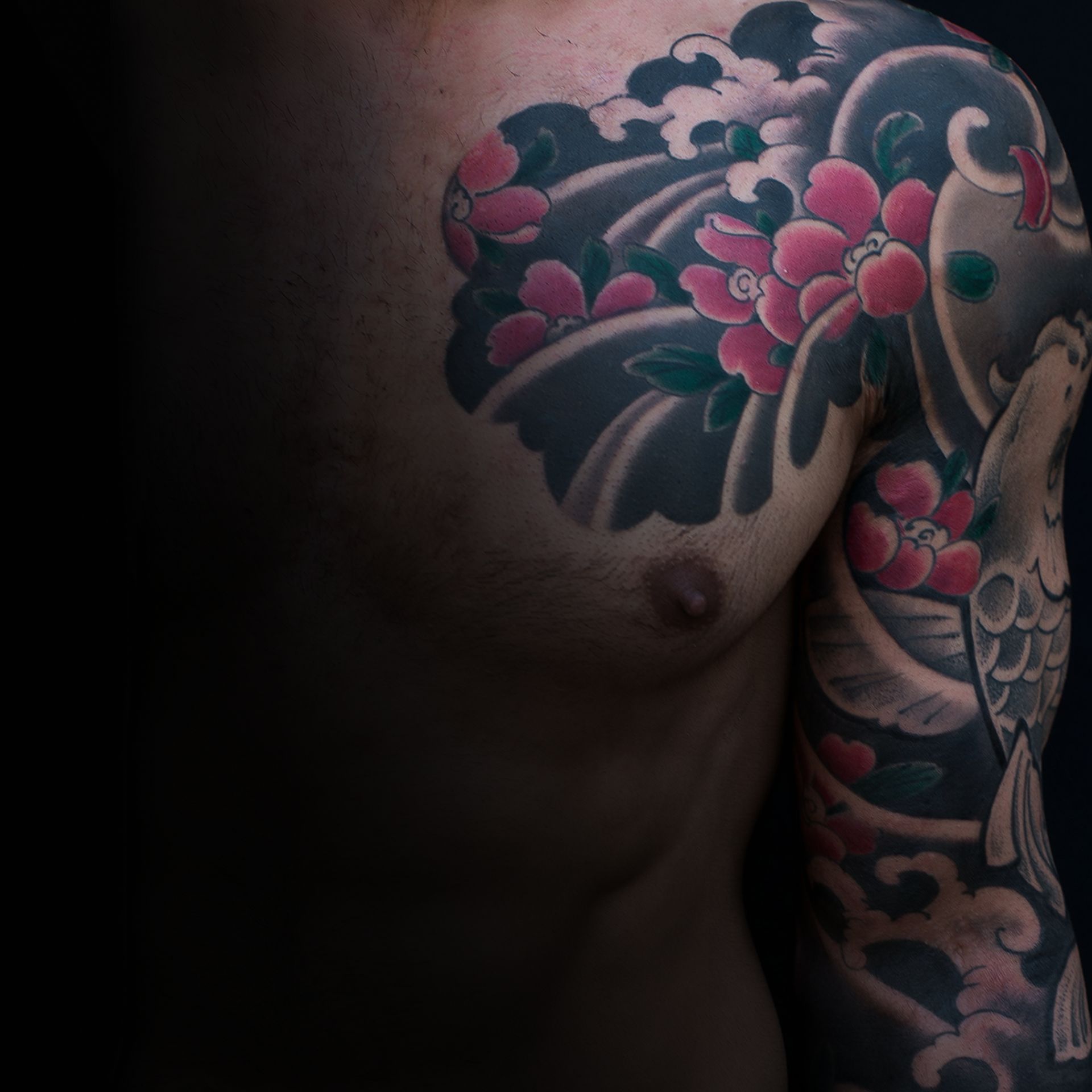 Tattoo on chest and arm, dark background. Cherry blossoms, waves, and a bird in a Japanese style.