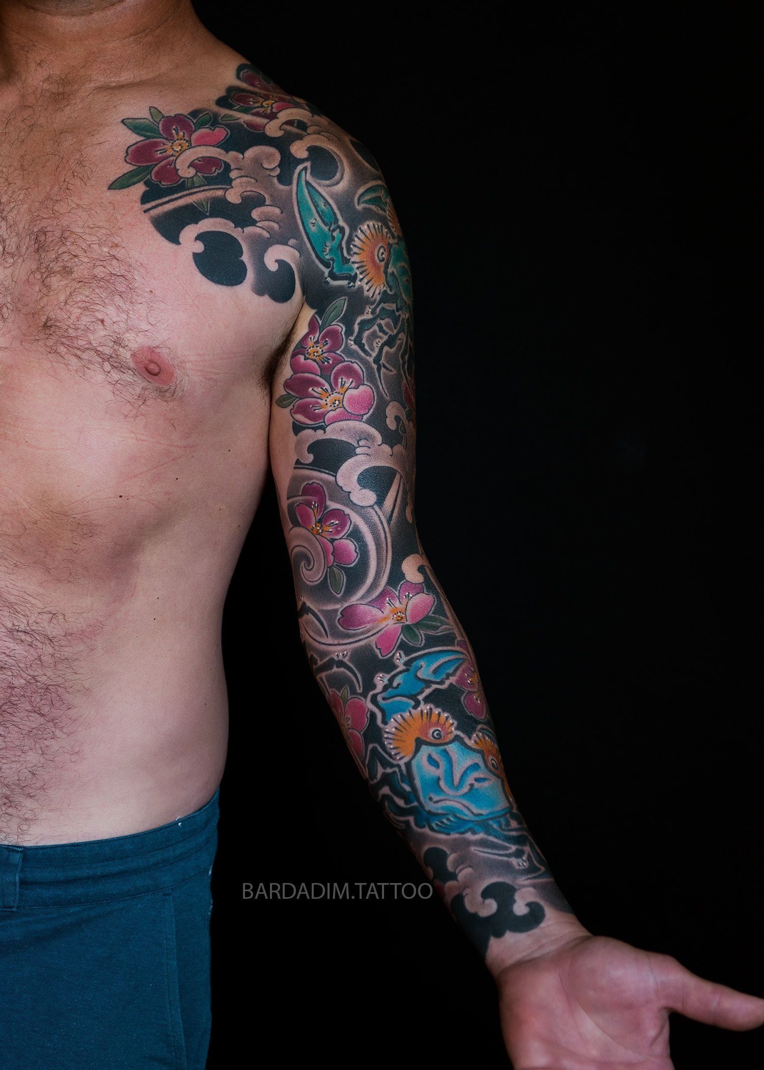 A shirtless man with a full sleeve tattoo on his arm.