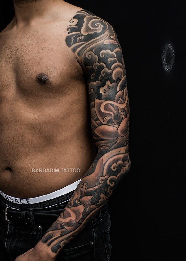 A shirtless man with a full sleeve tattoo on his arm.