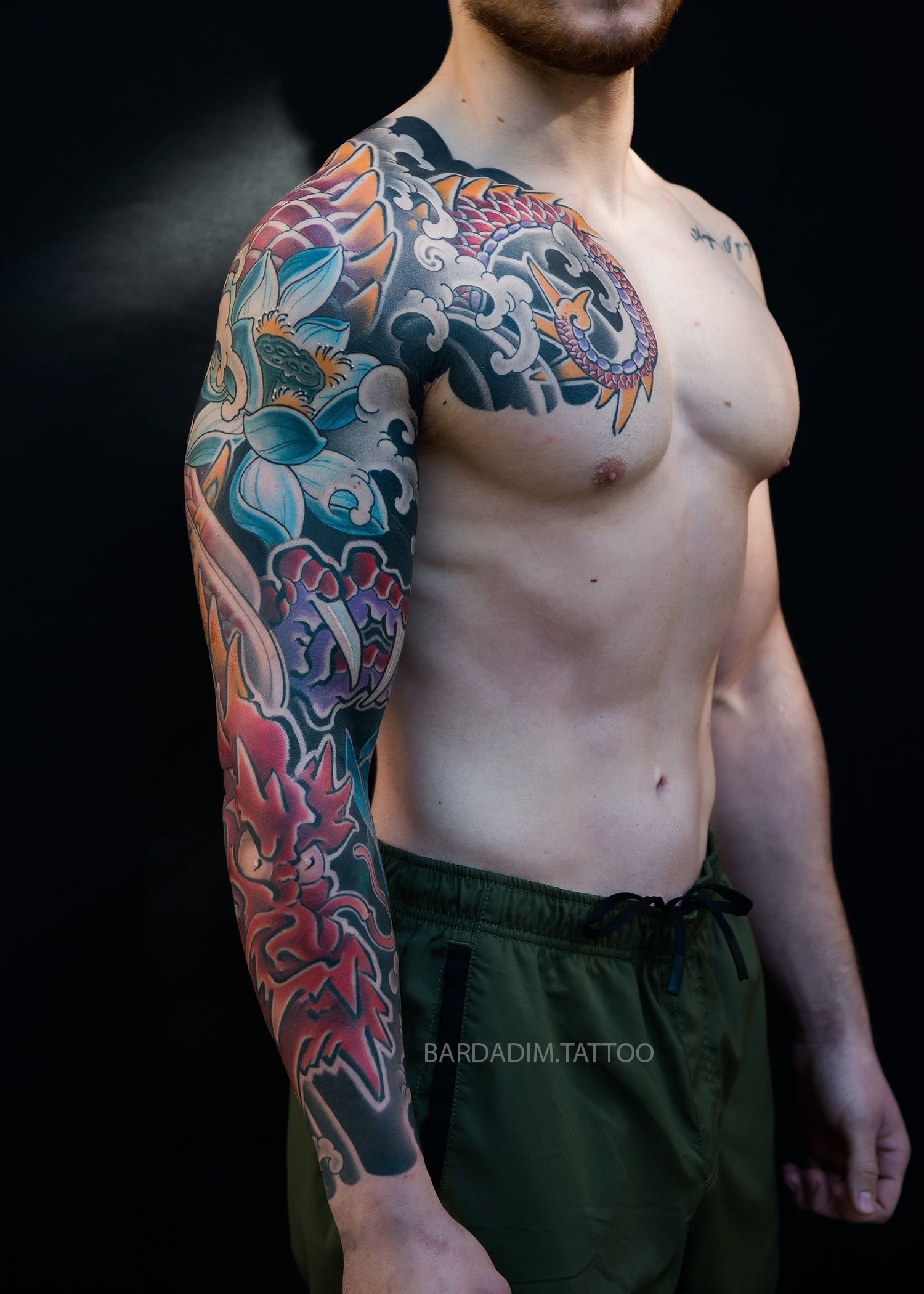 A shirtless man with a colorful tattoo on his arm and chest.