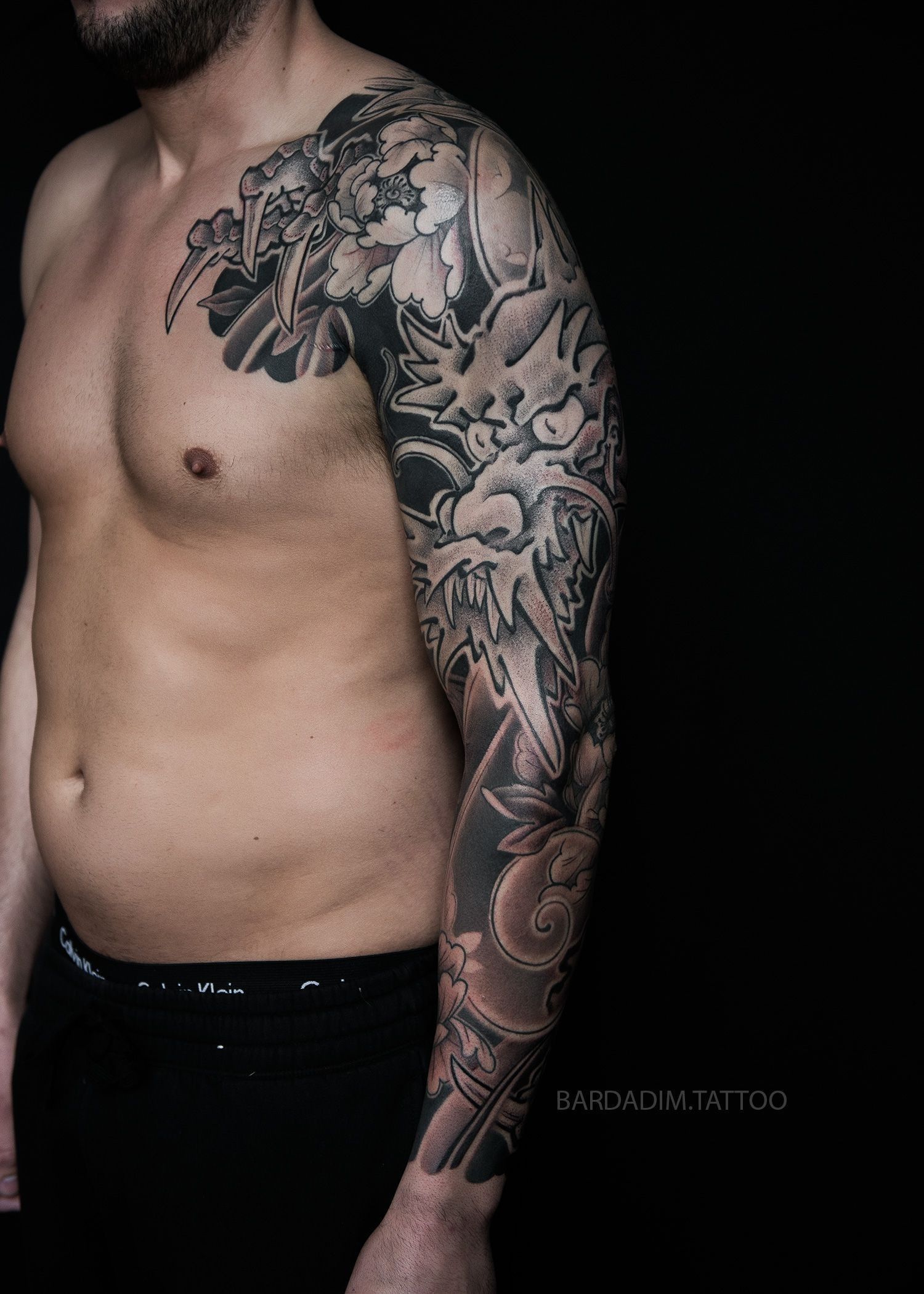 A shirtless man with a full sleeve tattoo on his arm.