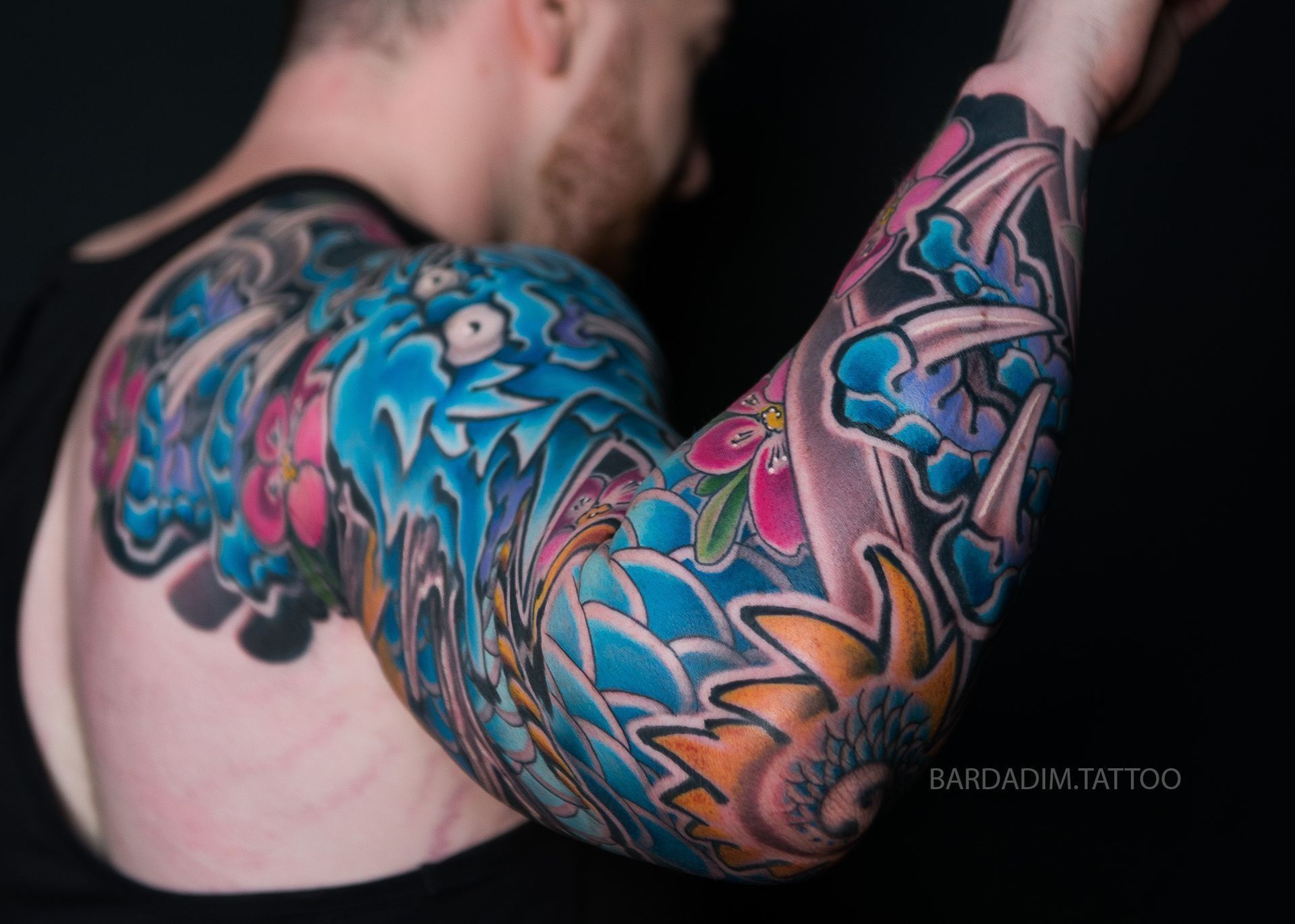 Man's arm covered in vibrant, intricate Japanese-style tattoo featuring blue water, flowers, and an eye.