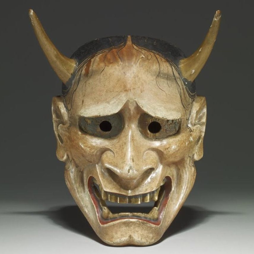 A close up of a demon mask with horns on a white surface