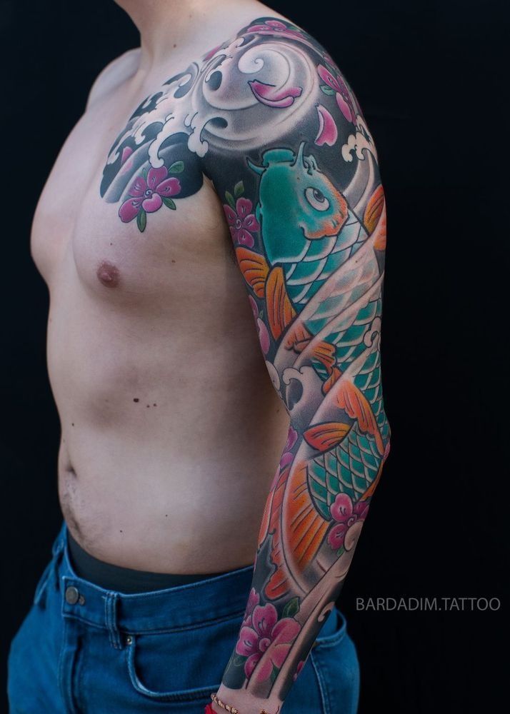 Man with a full sleeve tattoo featuring koi fish, waves, and cherry blossoms; colorful design.