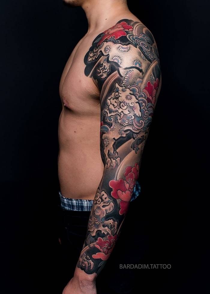 A shirtless man with a full sleeve tattoo on his arm.