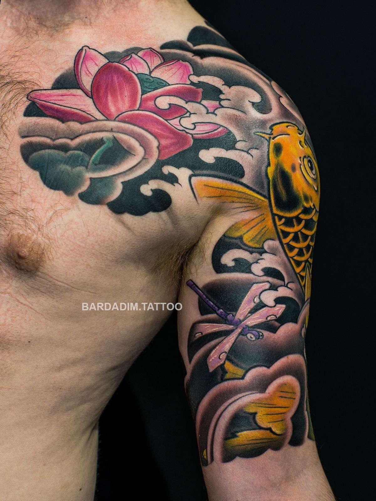 A man has a tattoo of a lotus flower and a fish on his shoulder.