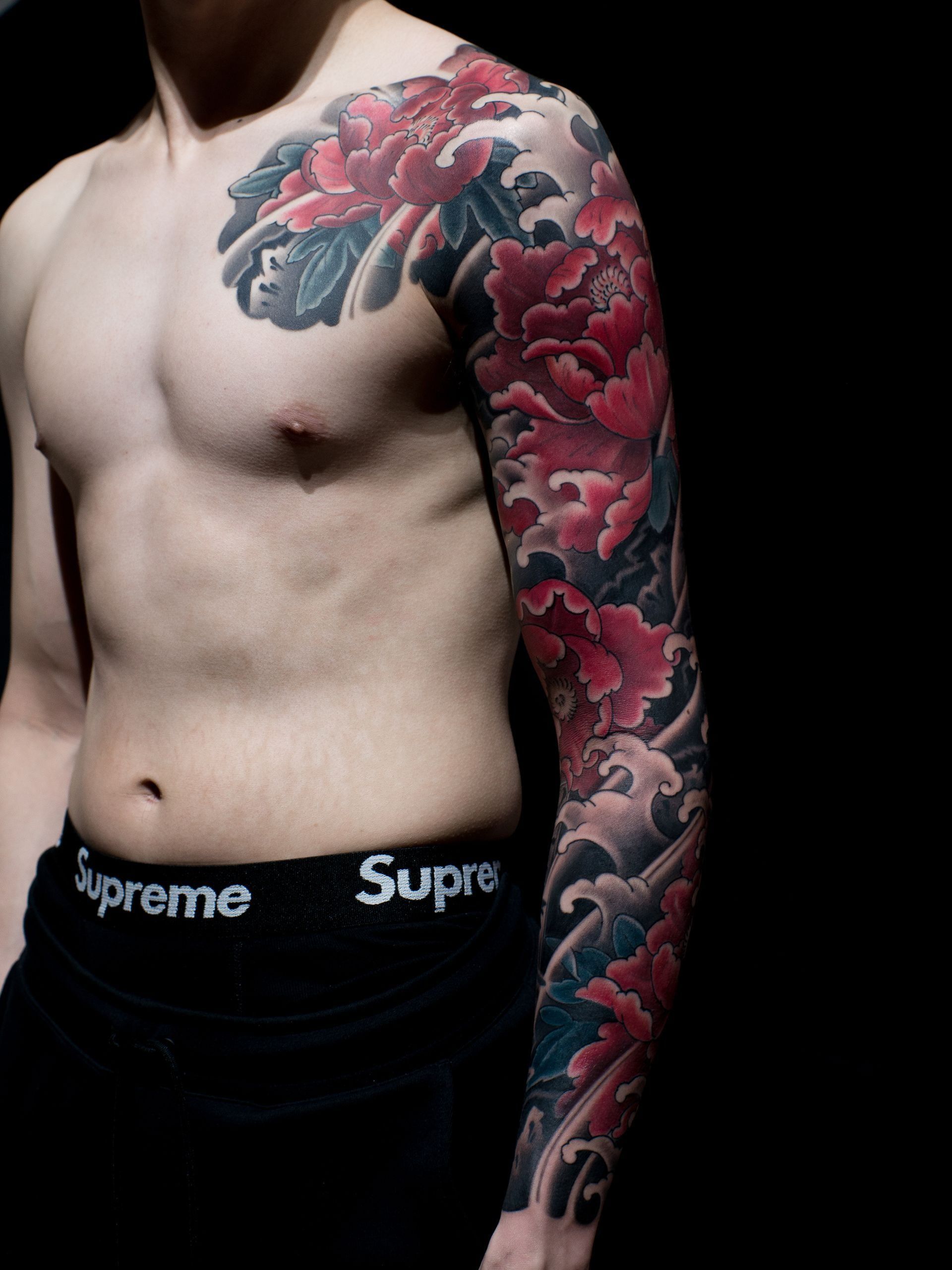 A shirtless man with a full sleeve tattoo and supreme underwear